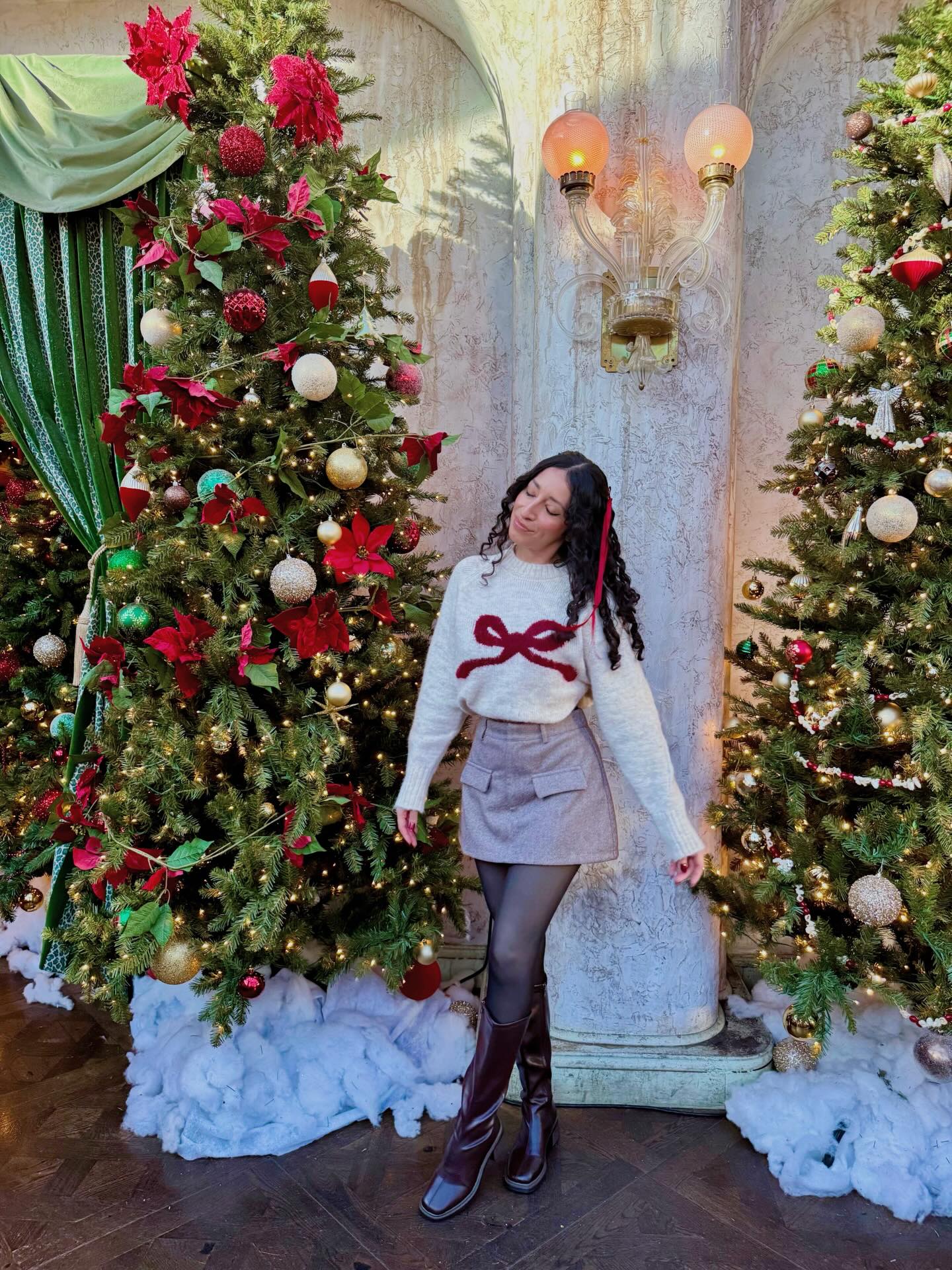 White Christmas sweater with red bow, gray mini skirt, dark tights and burgundy knee-high boots.