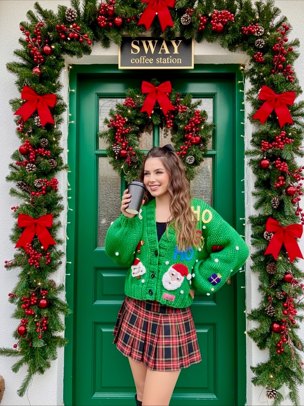 Festive ugly Christmas cardigan outfit with a green Santa cardigan, red plaid mini skirt, and black boots.