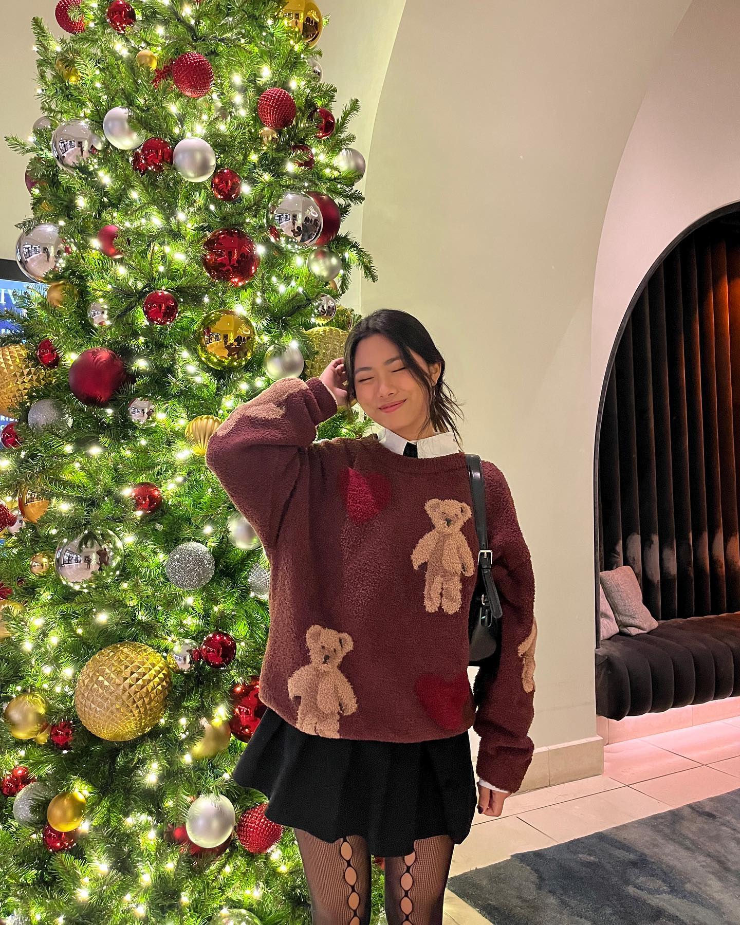 Christmas sweater outfit with a brown teddy bear knit, white collared shirt, black mini skirt, and patterned tights.