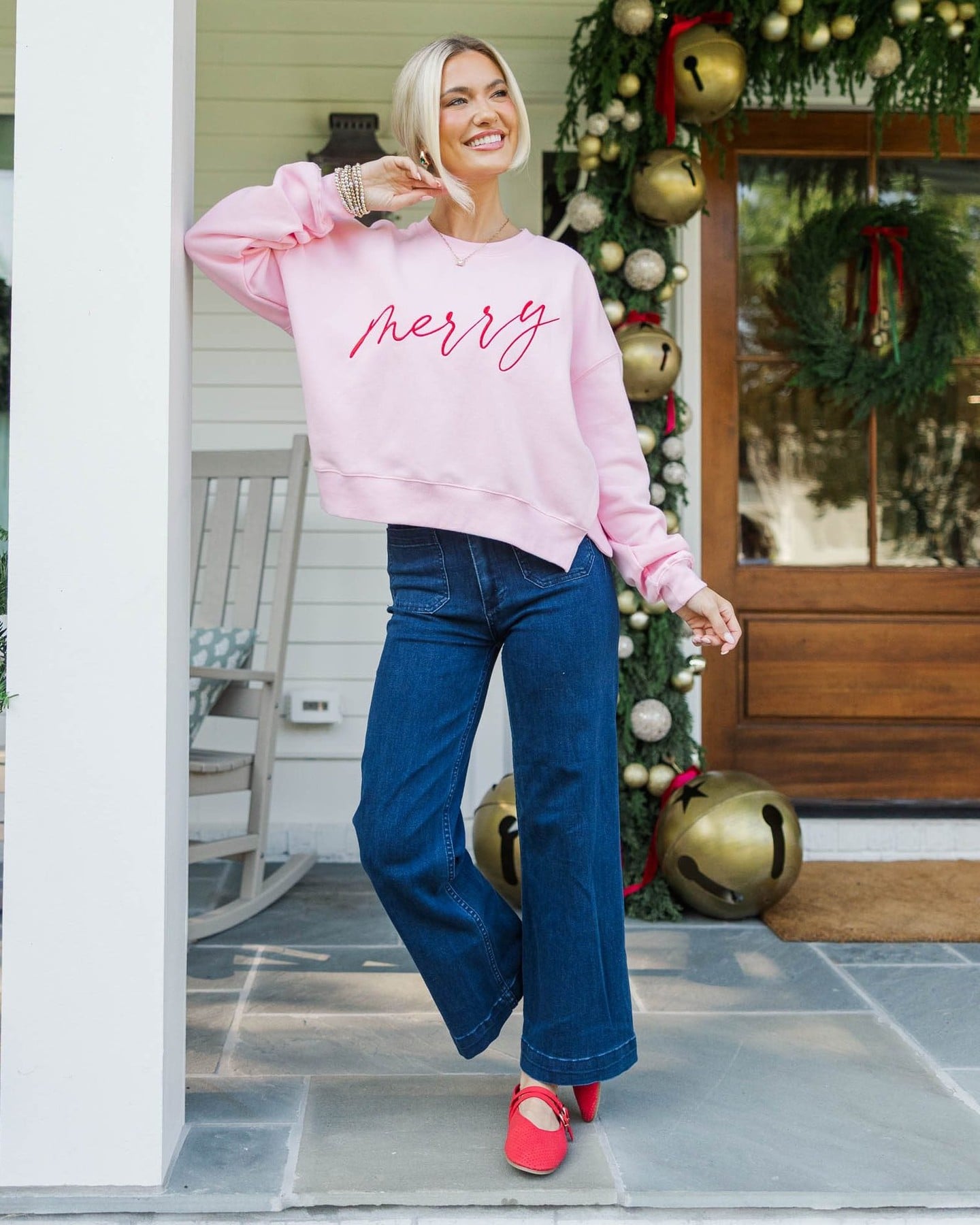 Casual Christmas outfit with a pink Merry sweatshirt, blue wide-leg jeans, and bright red Mary Jane flats.
