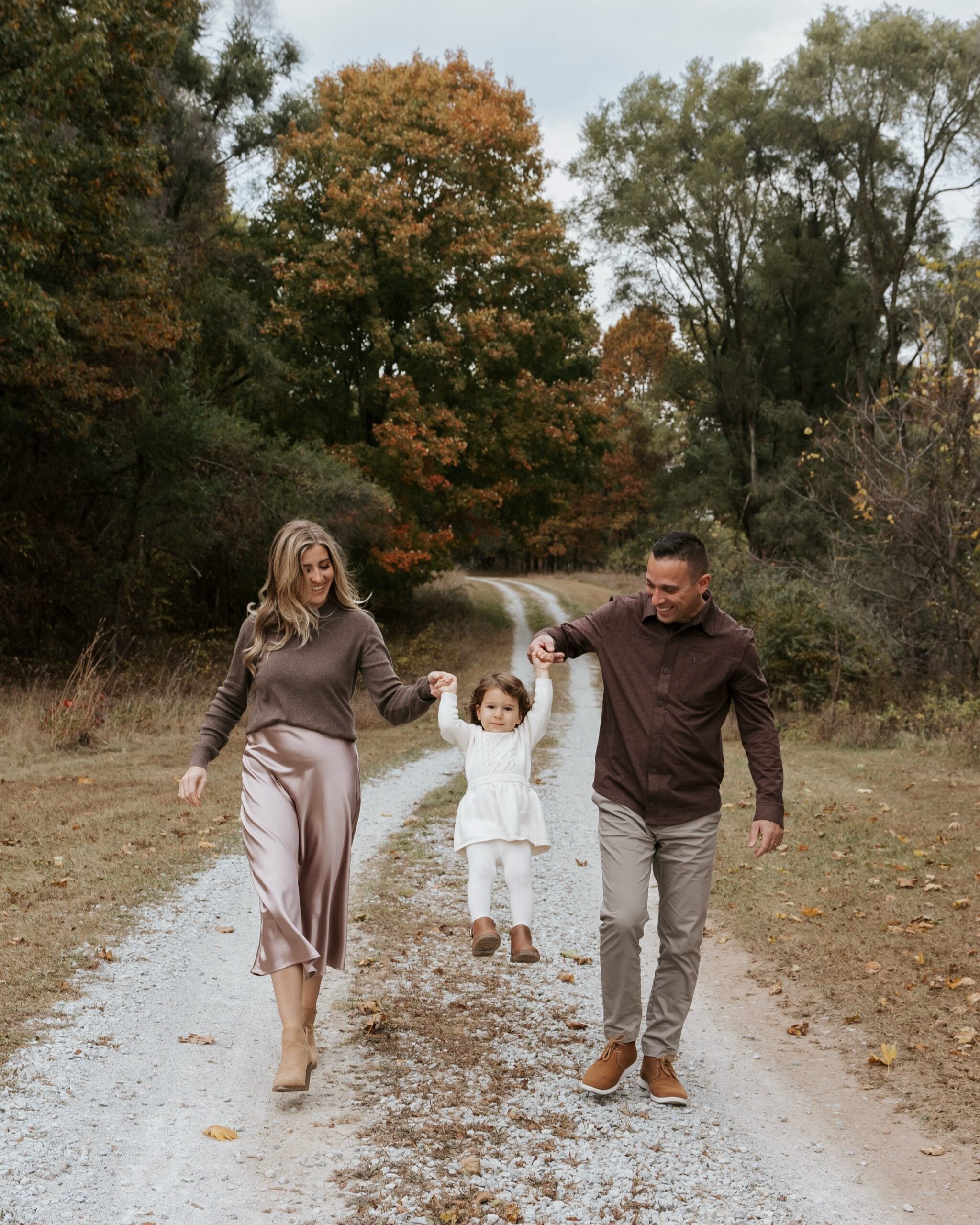 Parents and daughter wearing taupe, chocolate brown and cream outfits for outdoor fall family pictures