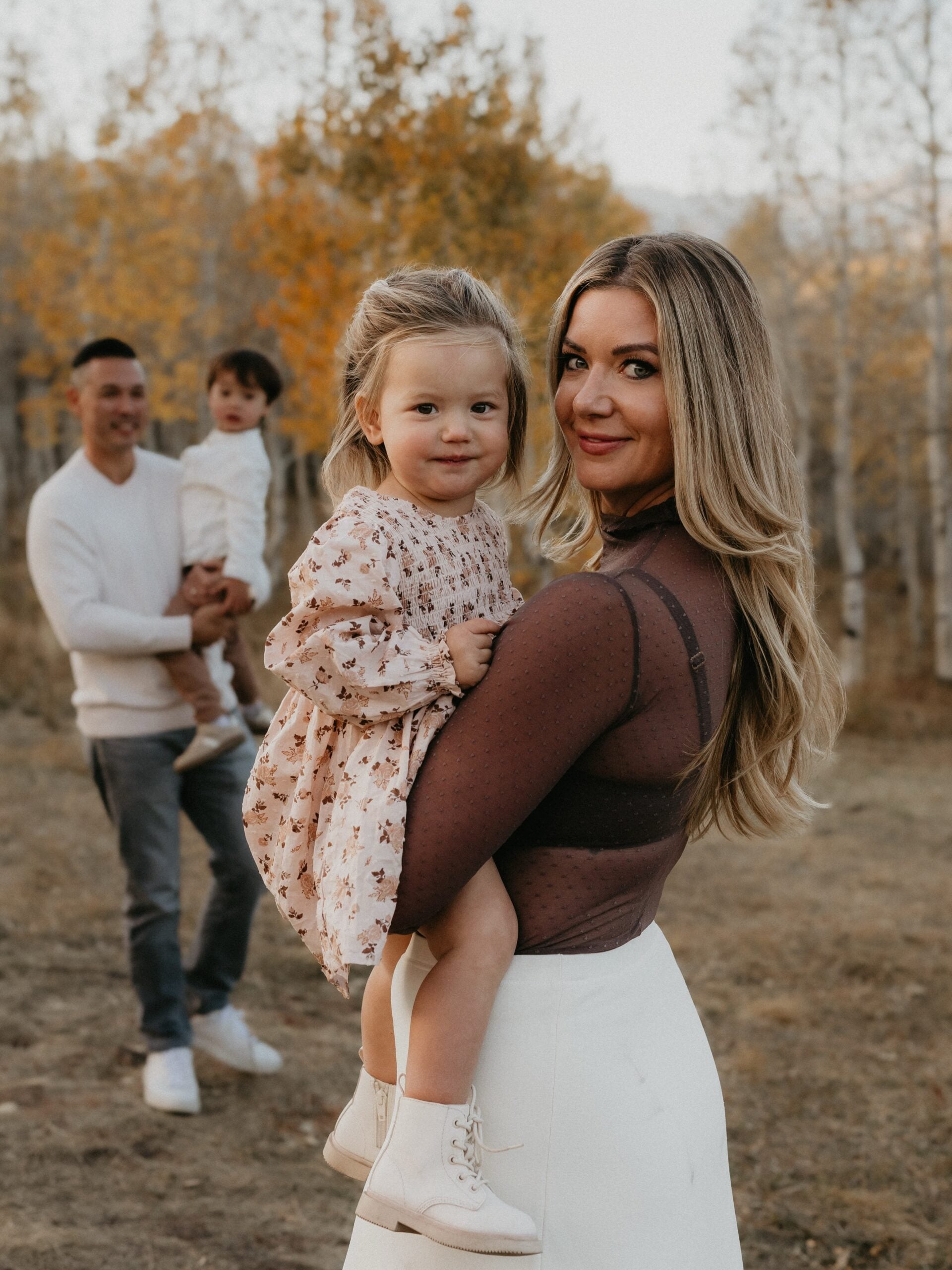 Mom wearing a brown top and white skirt while holding her daughter in a floral dress during a fall family photoshoot