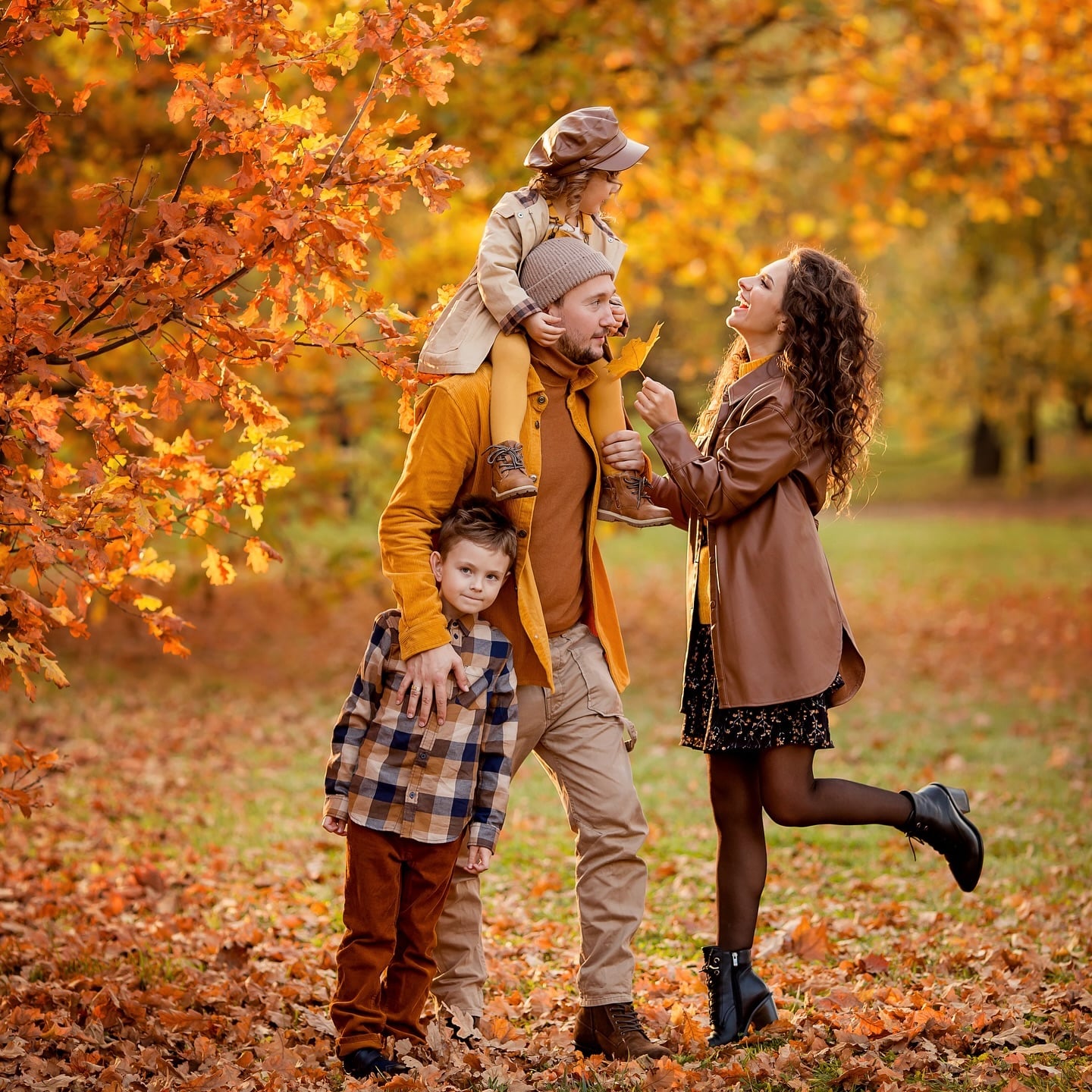 Family of four wearing mustard, camel, brown and plaid outfits among orange fall leaves