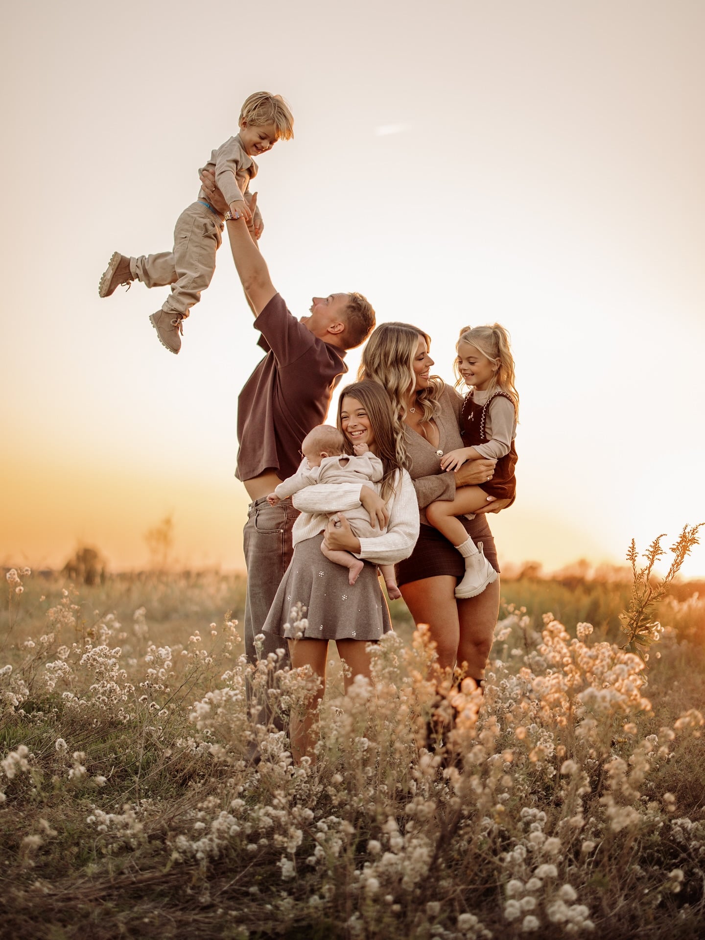 Family of six wearing cream, taupe and brown fall family picture outfits in a wildflower field at sunset