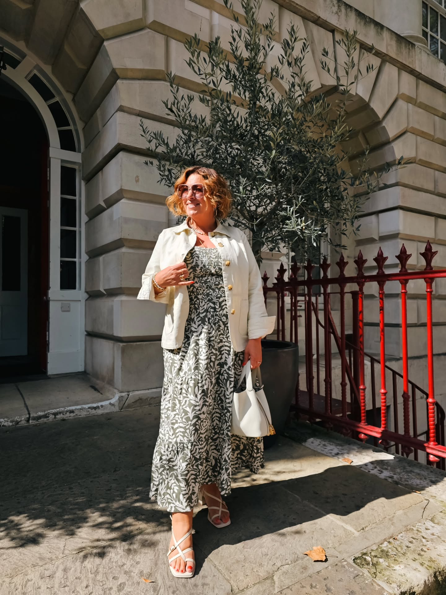 Green printed dress with a cream jacket, an outfit idea for women over 50 who prefer arm coverage.