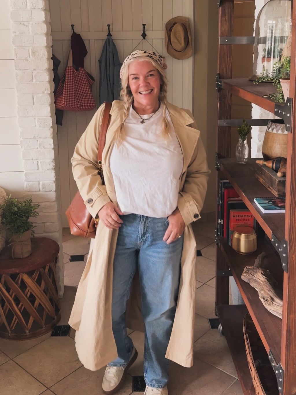 Casual jeans outfit for women over 50 with a beige trench coat, white top, and relaxed jeans.
